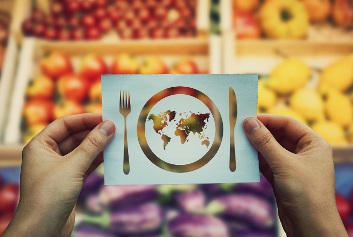 Image of fresh fruit and vegetables with a stencil of a plate, knife and fork with a world map cut out on the plate.