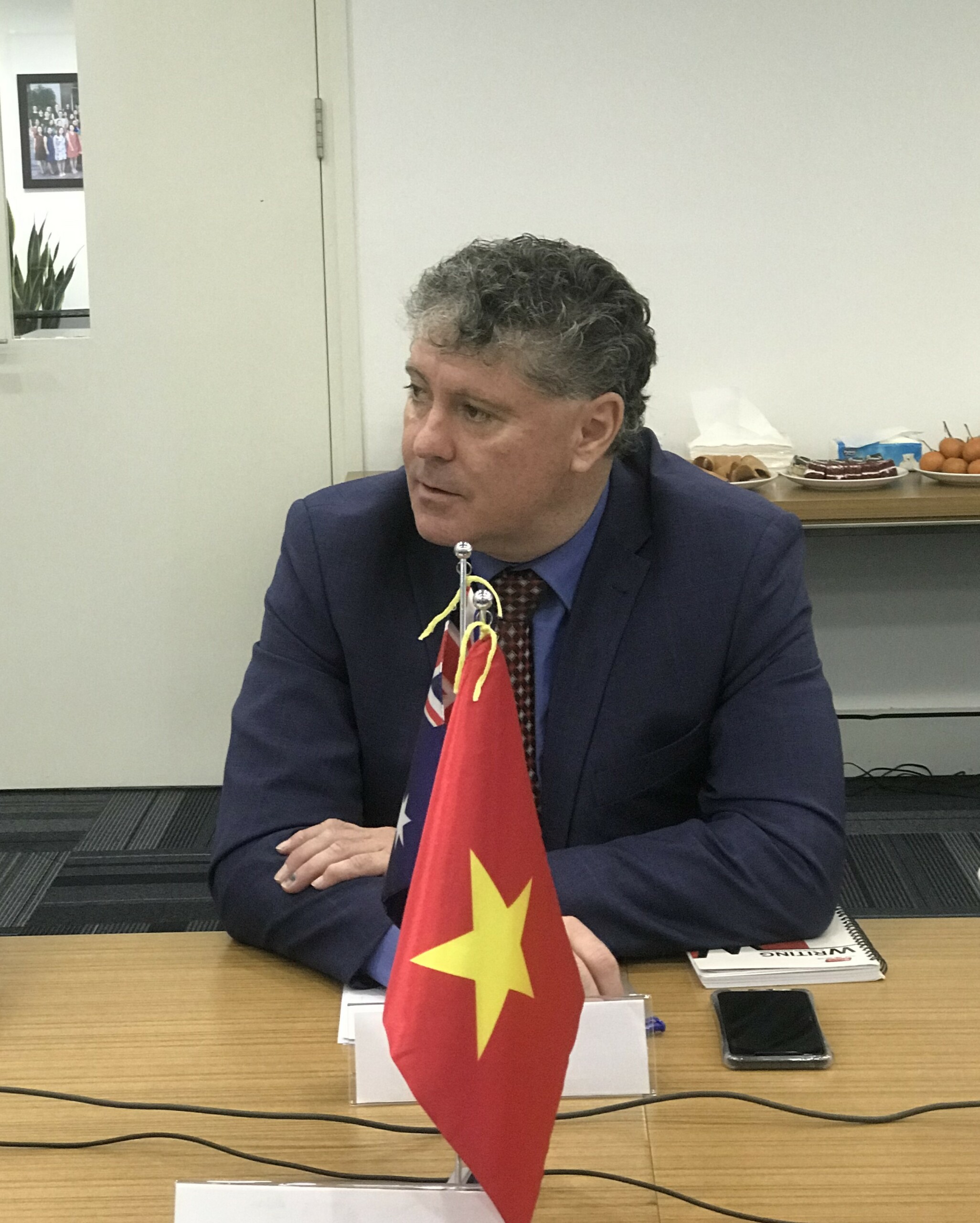 A photo of Tony Harman sitting behind an Australian and Vietnamese flag
