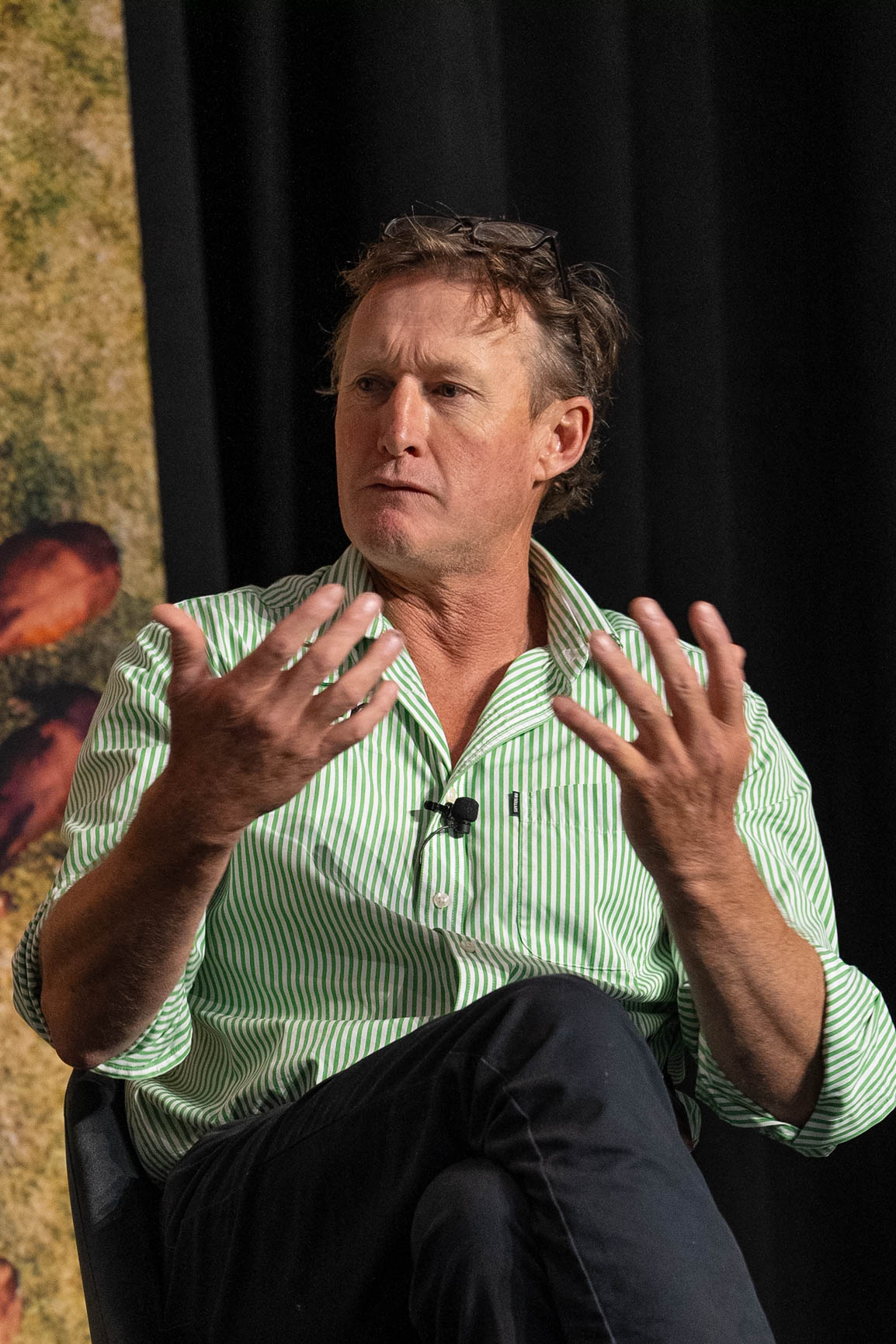 Man wearing a green striped shirt talking on stage and using his hands.