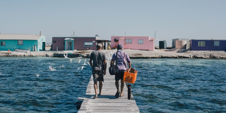Two people walking on a jetty with their seafood catch in hand.