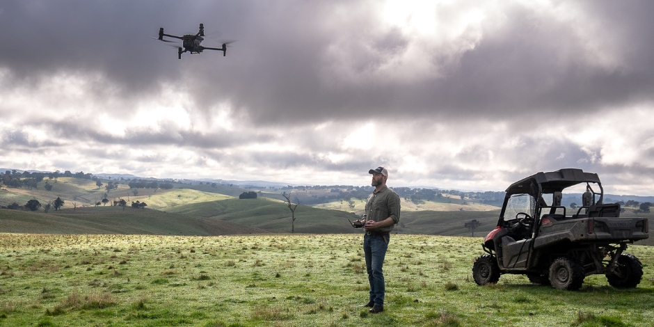 Australian farmer flying an agricultural drone over green paddocks with a utility vehicle parked nearby, using drone technology for modern farming practices under cloudy skies